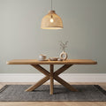 Wooden dining table with decorative items under a woven pendant light against a plain wall.