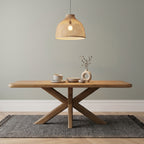 Wooden dining table with decorative items under a woven pendant light against a plain wall.
