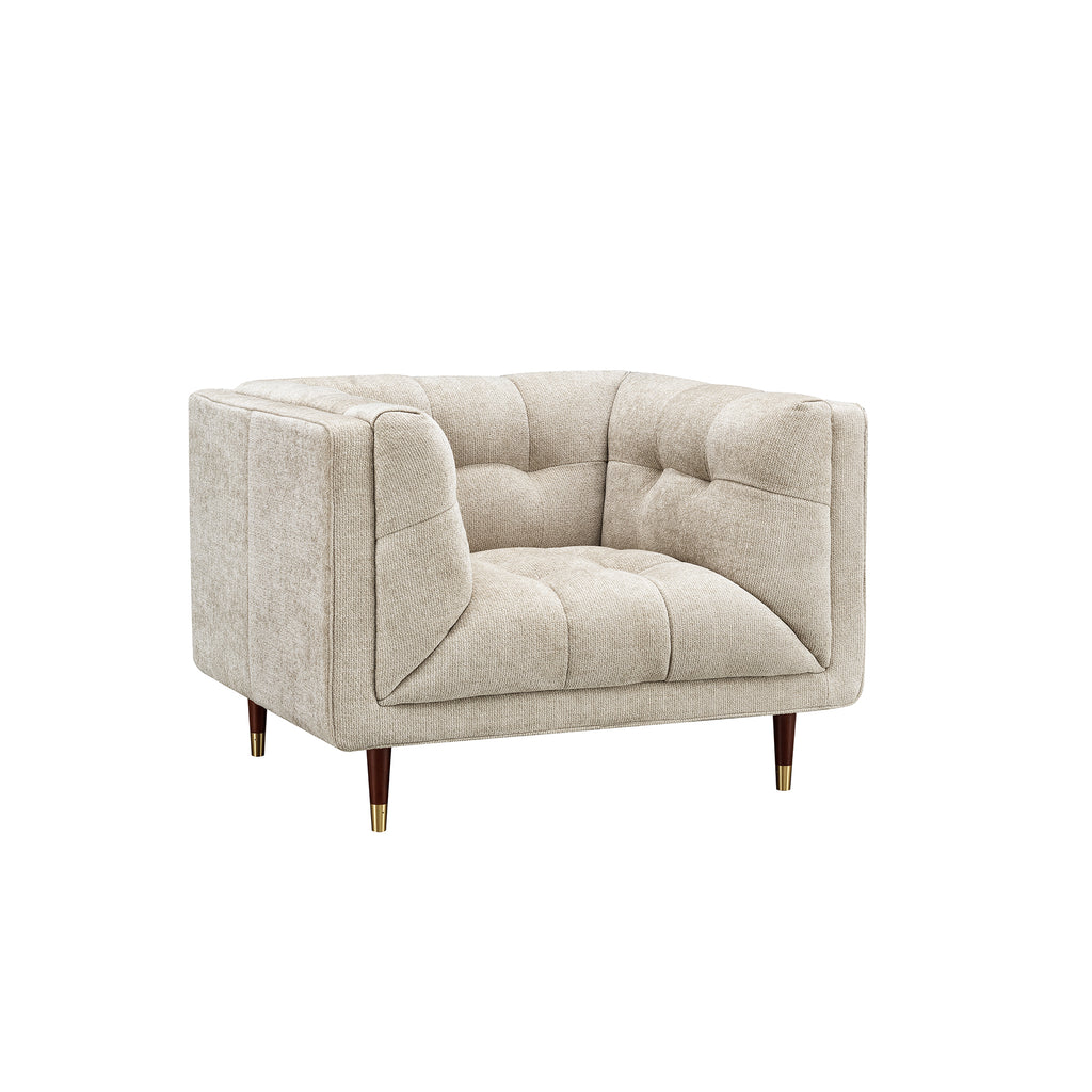 A modern tufted armchair in a textured light beige fabric, featuring dark brown wooden legs with gold-toned metal caps, shown against a plain white background.