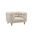 A modern tufted armchair in a textured light beige fabric, featuring dark brown wooden legs with gold-toned metal caps, shown against a plain white background.