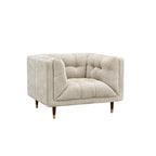A modern tufted armchair in a textured light beige fabric, featuring dark brown wooden legs with gold-toned metal caps, shown against a plain white background.