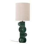 A modern table lamp with a cylindrical off-white fabric shade and a sculptural dark green ceramic base featuring circular and rectangular forms.