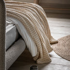 Beige textured blanket draped over a white chair on a wooden floor.