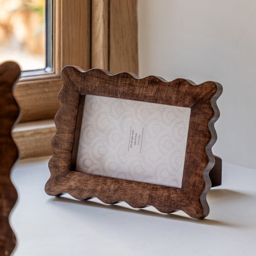Wooden photo frame with scalloped edges on a white surface.