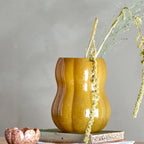 Brown ceramic vase with decorative elements on a wooden surface against a grey background