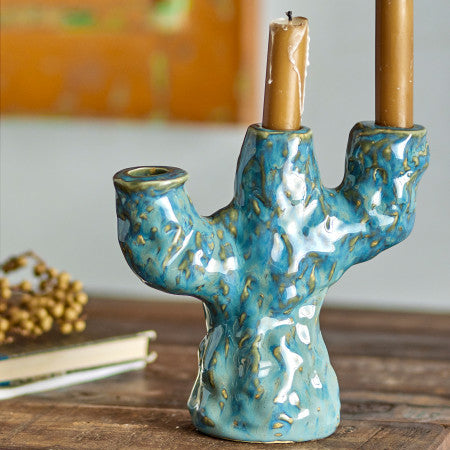 Ceramic cactus-shaped candle holder with two candles on a wooden surface.
