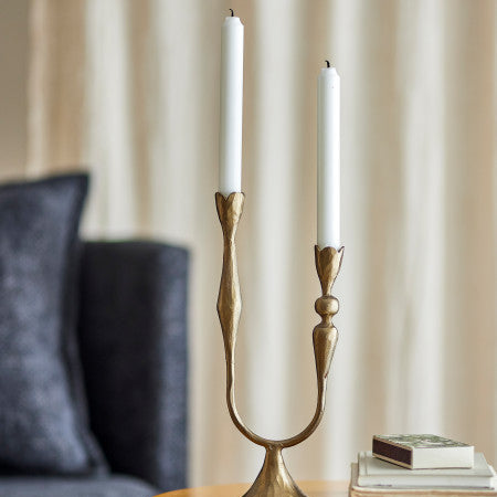 Gold candle holder with two white candles on a table against a neutral background