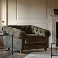 Green velvet sofa in a living room setting with a fireplace and coffee table.