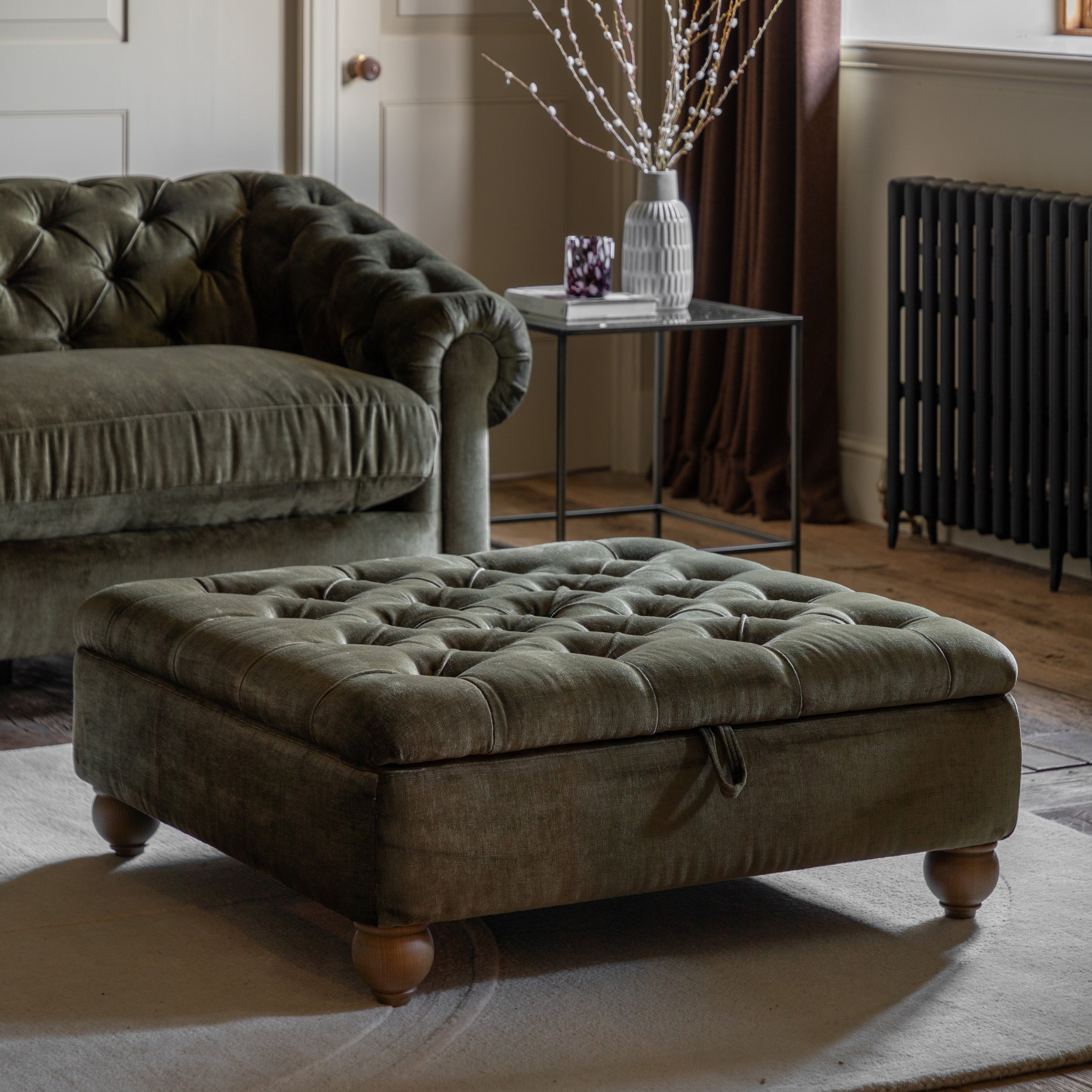 Green tufted ottoman in a living room setting with a sofa and decorative items.