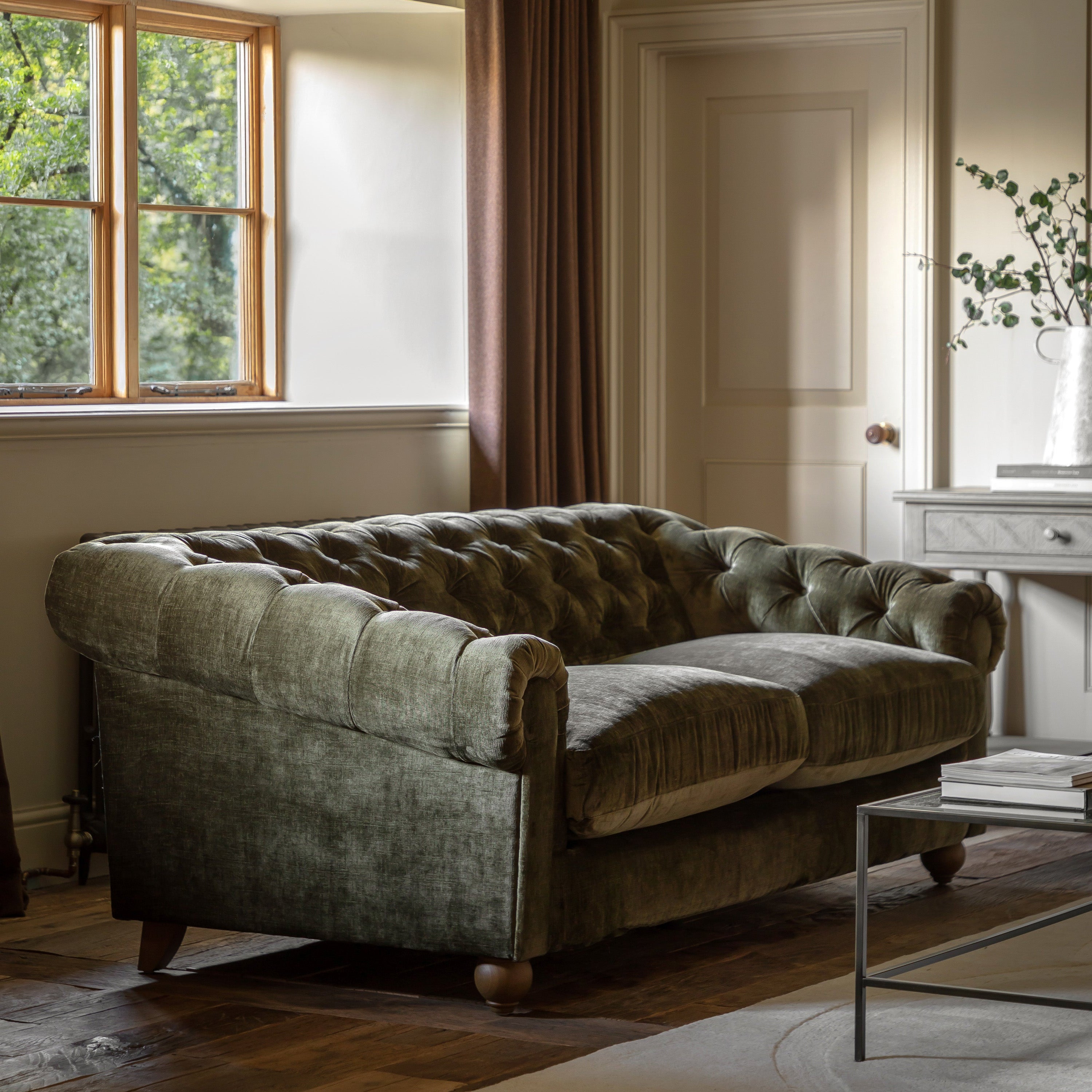 Green velvet sofa in a room with a window and side table.