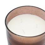 Close-up of a white candle in a glass container with a speckled brown base