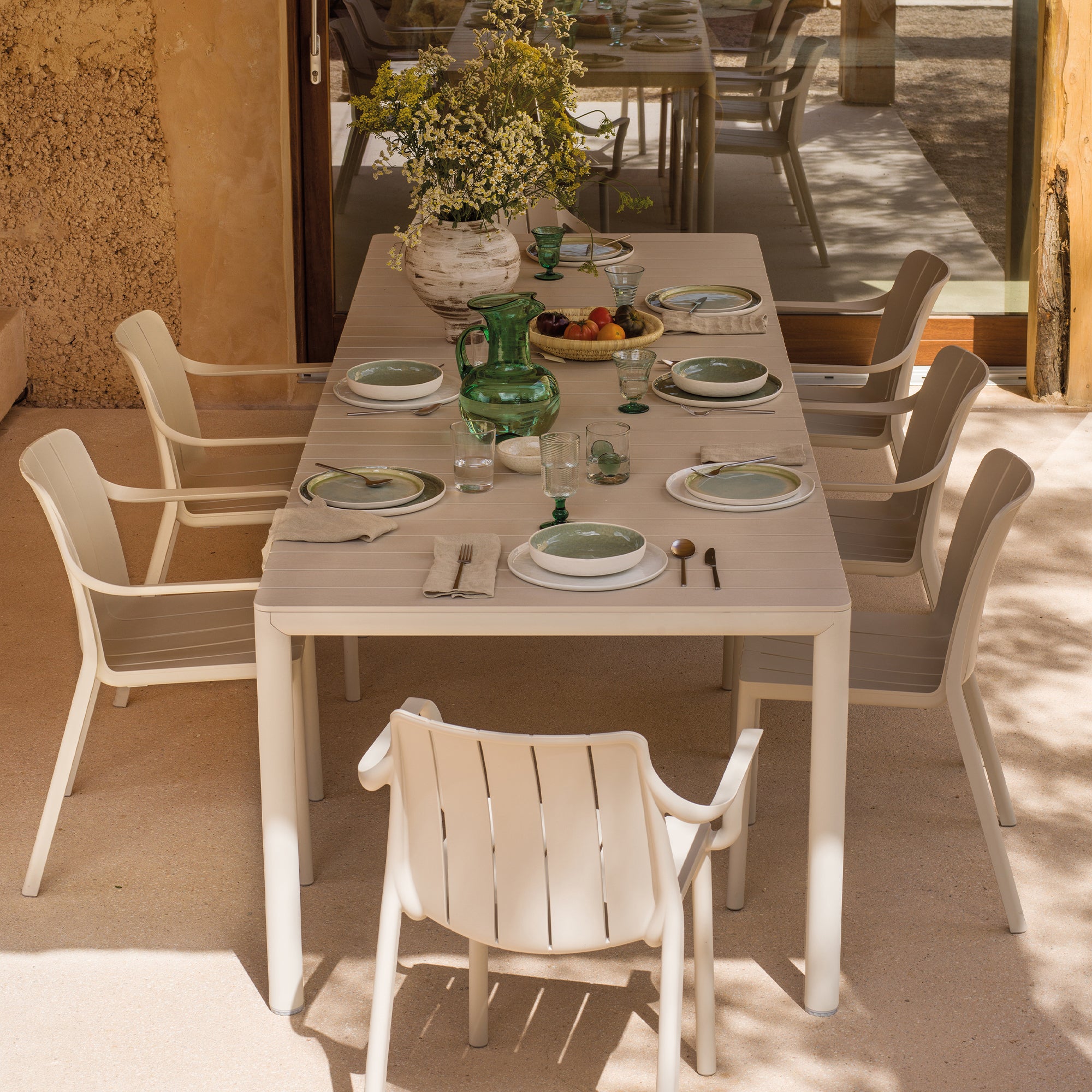 Tevere dining table set with plates, glasses, and cutlery on a patio with chairs around.