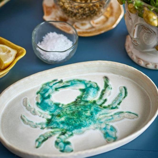 Ceramic plate with a green crab design on a blue surface with condiments.