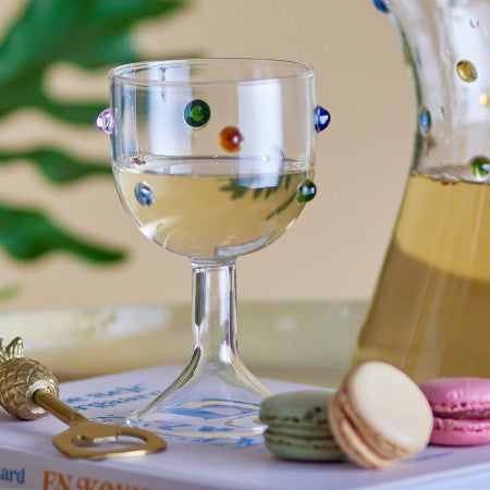 Wine glass with colourful dots, a bottle of wine, and macarons on a table creating the perfect room set