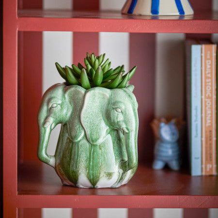 Green elephant-shaped vase with succulents on a red shelf with striped wall