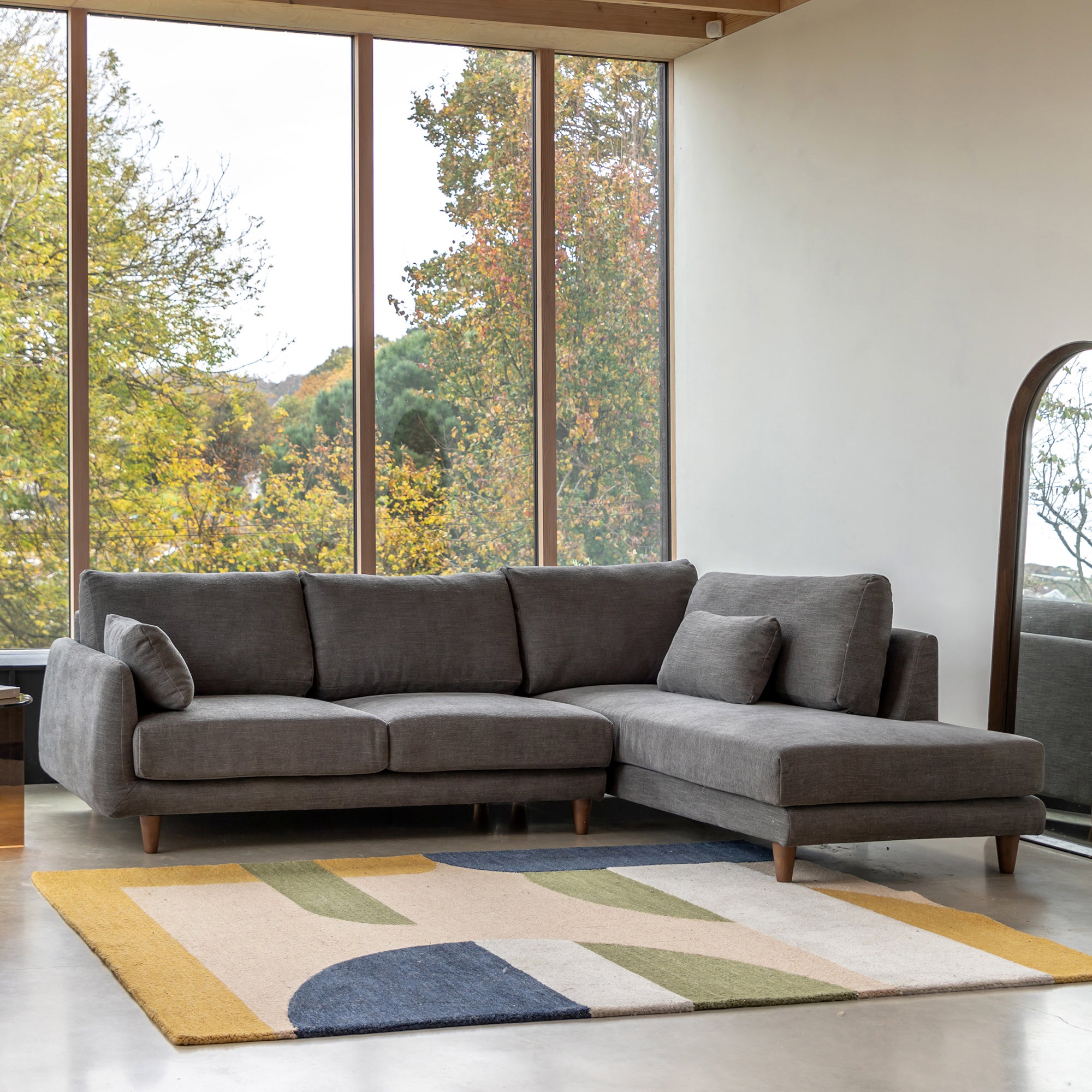 Gray Eva sectional sofa right hand facing in a room with large windows and a colorful rug.