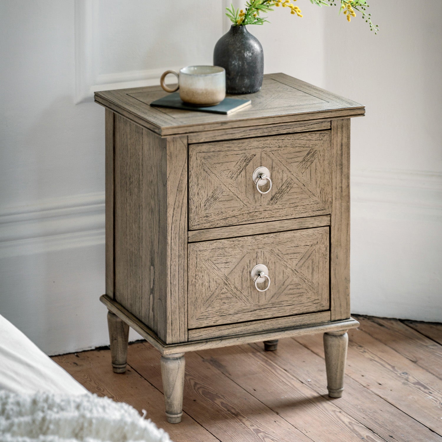 Faringdon 2 Drawer Bedside Table in a styled bedroom setting next to a bed, demonstrating its functionality for night-time essentials and decorative items