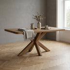 Wooden dining table with cross-leg design in a room with a window and grey wall.