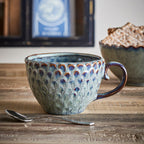 Ceramic mug with textured design on a wooden surface, with a blurred background