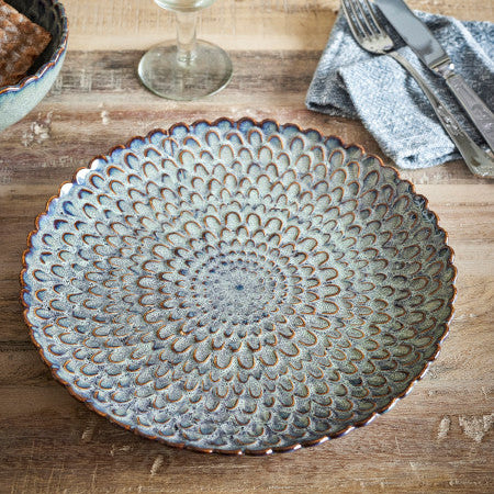 Decorative ceramic plate on a wooden table with a glass of water and cutlery.