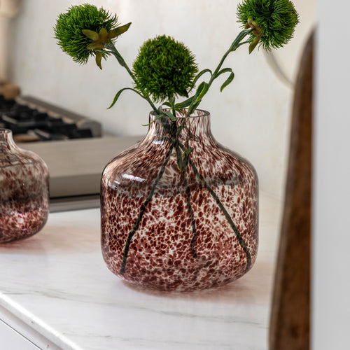 Brown vase with green flowers on a kitchen counter