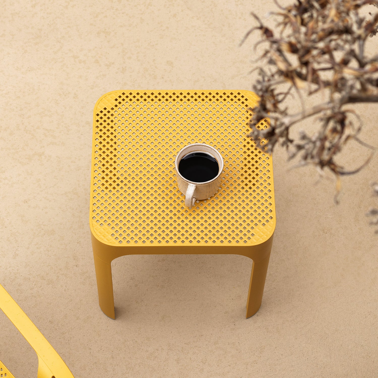 Yellow net 40 side table with a textured surface featuring a cup of coffee on a beige background.