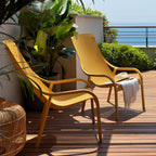 Two yellow net lounge chairs on a wooden deck with plants and a hat.
