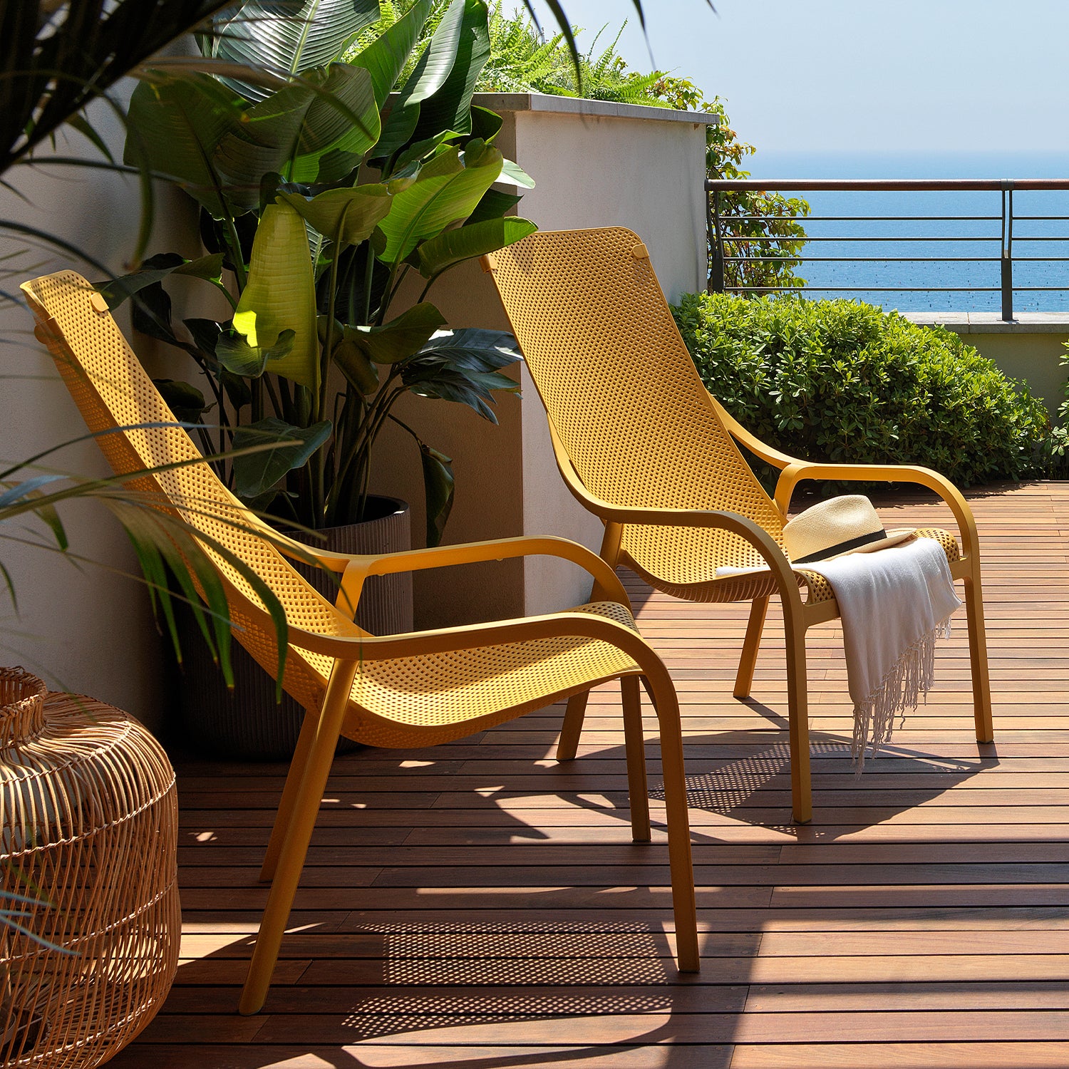 Two yellow net lounge chairs on a wooden deck with plants and a hat.