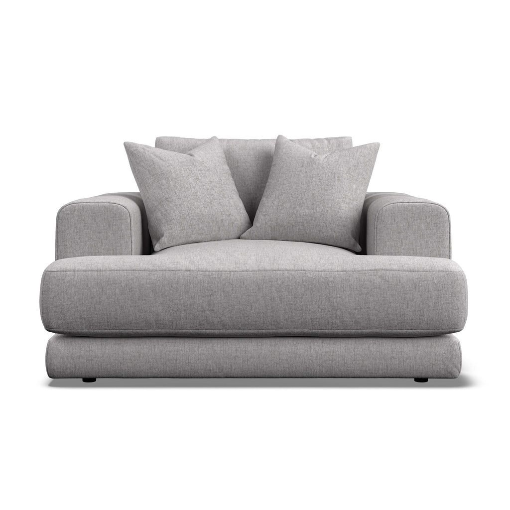 A modern low-profile armchair in light gray textured fabric, featuring two matching throw pillows, shown against a plain white background.