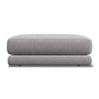 A light gray upholstered ottoman or low stool with a thick rectangular seat cushion and rounded legs, shown against a plain white background.