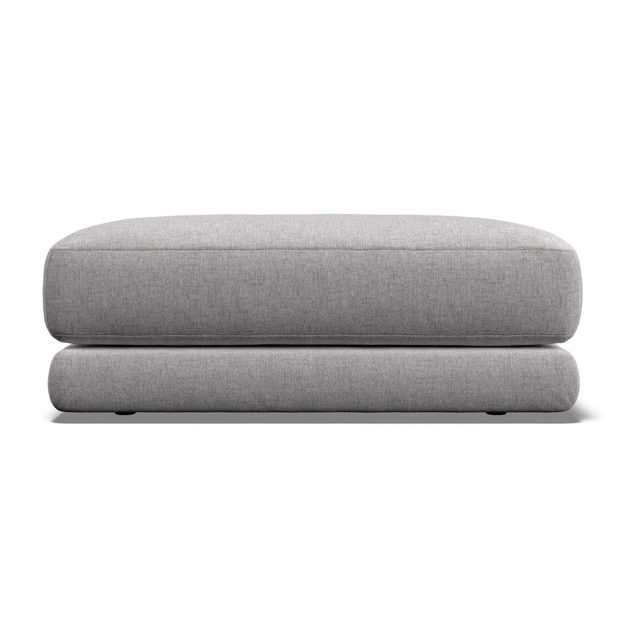 A light gray upholstered ottoman or low stool with a thick rectangular seat cushion and rounded legs, shown against a plain white background.