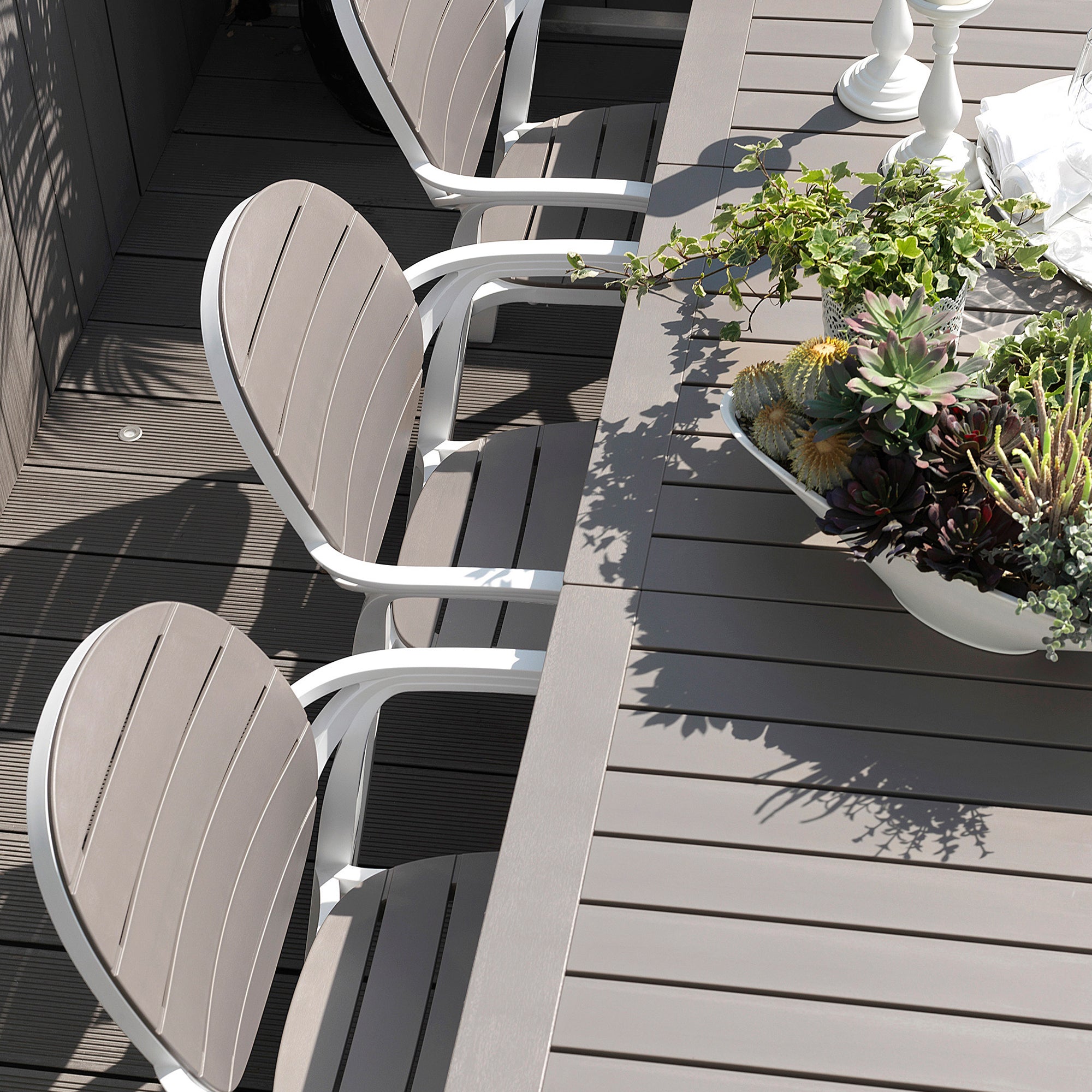Outdoor furniture set with chairs and a table on a wooden deck, featuring plants.