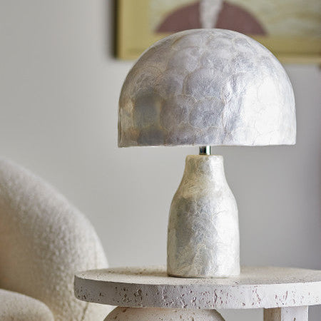 Room set for a pearl table lamp on a surface with a blurred artwork in the background