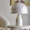 Room set for a pearl table lamp on a surface with a blurred artwork in the background