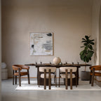 Dining room with Walnut table and chairs, abstract painting on the wall, and a plant.