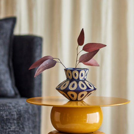 Yellow table with a decorative vase and plant against a beige curtain creating a room set
