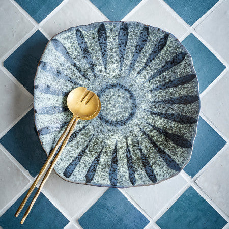 Decorative ceramic plate with gold fork on a grey tiled surface