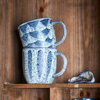 Two grey ceramic mugs stacked on a wooden shelf with a textured finish.