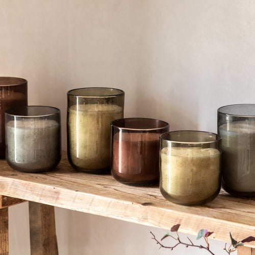 Set of glass candle holders in various colors on a wooden shelf.