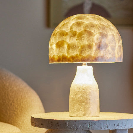 Table lamp with a textured glass shade on a concrete base in a room setting.
