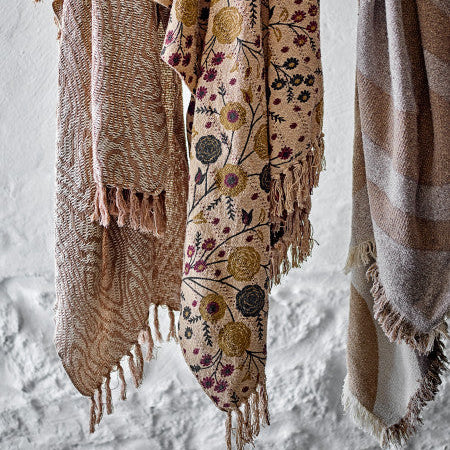 Three patterned throws hanging on a wooden rod against a textured white wall creating a room set