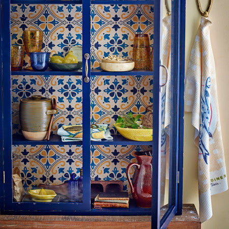 Blue cabinet with decorative tiles and various items inside, including a towel hanging on the right.