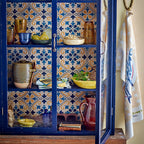 Blue cabinet with decorative tiles and various items inside, including a towel hanging on the right.