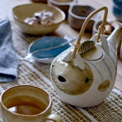 Ceramic teapot and cup on a textured surface with a woven mat