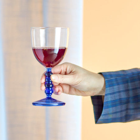 Hand holding a blue glass with red liquid against a neutral background