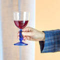 Hand holding a blue glass with red liquid against a neutral background