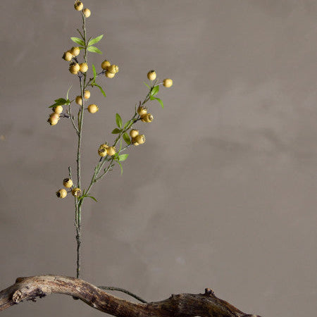 Artificial plant with yellow berries on a wooden branch against a gray background