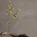 Artificial plant with yellow berries on a wooden branch against a gray background